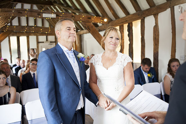 Bride and groom holding hands and looking at the registrar