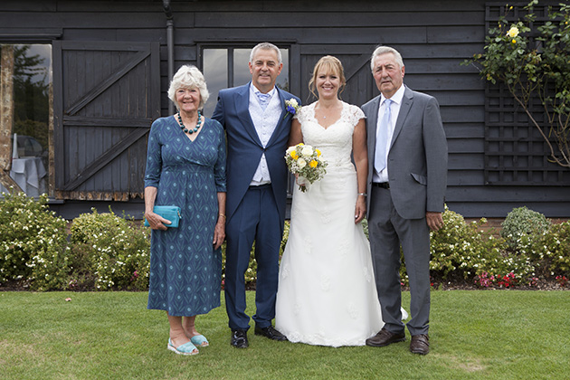 Small wedding group photo on grass outside barn