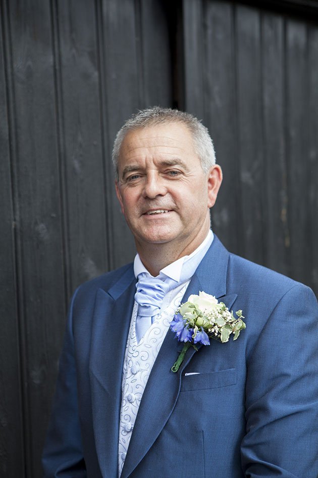 Portrait of groom against painted black wooden slats of barn