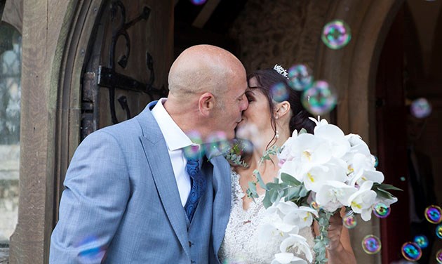 Married couple kissing in doorway of church with bubbles