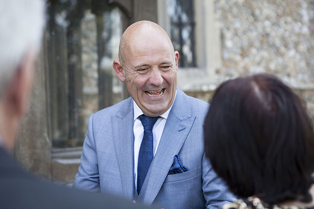 Candid photo of groom laughing with guest outside church