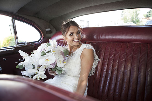 Bride sitting on red leather seat in back of car and looking to the side