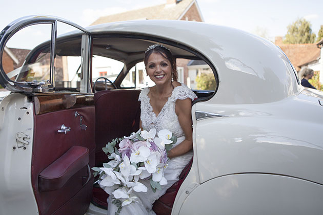 Portrait of bride sitting in doorway of wedding car with door open