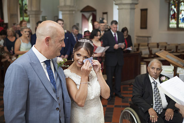 Bride standing with groom during ceremony and wiping her eye