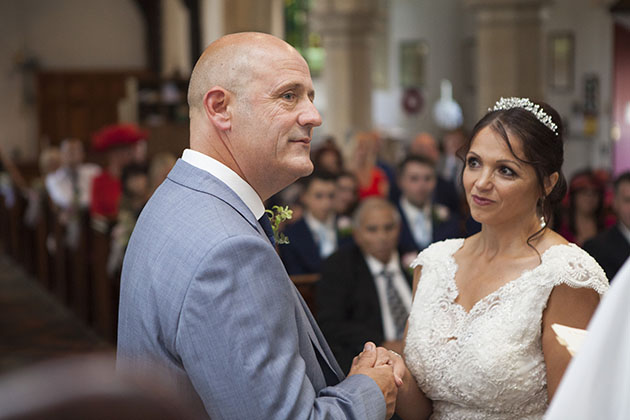 Groom holding bride's hand and looking at vicar during wedding ceremony