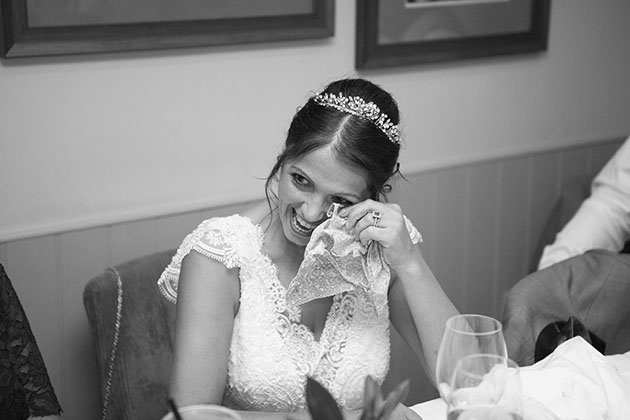 Bride sitting at table and wiping her eye during speeches at wedding reception