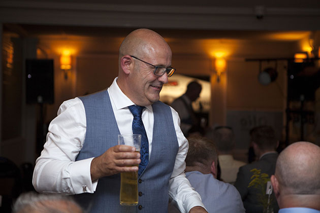 Groom carrying pint of beer and walking between tables at wedding reception